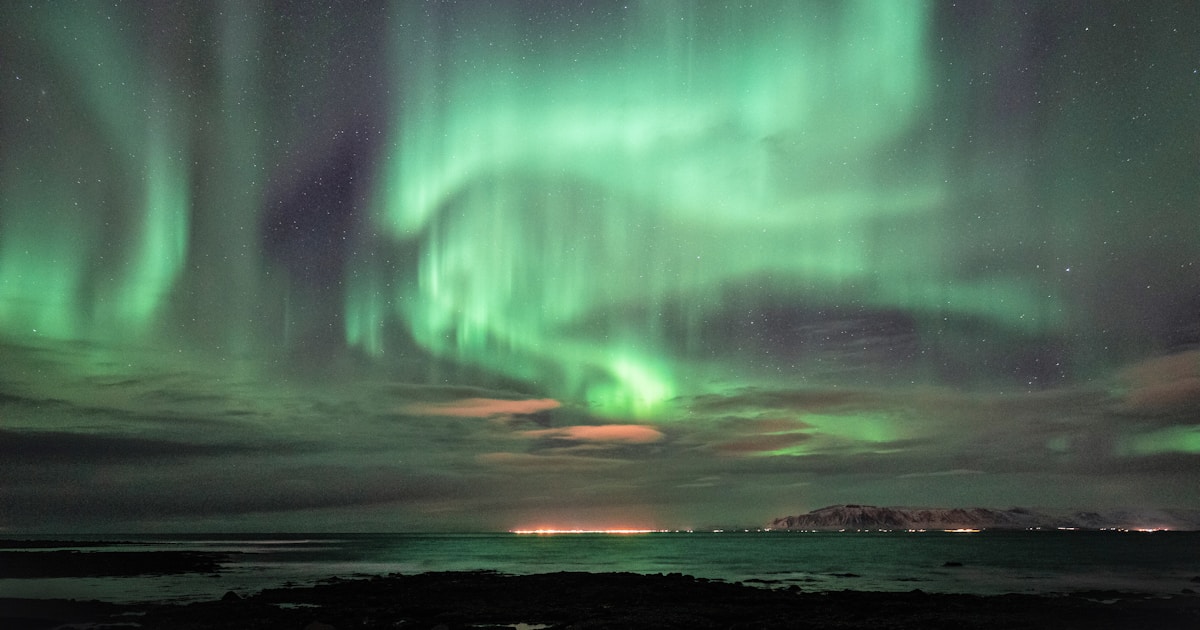Green and blue aurora borealis over the Reykjavik coastline, Iceland